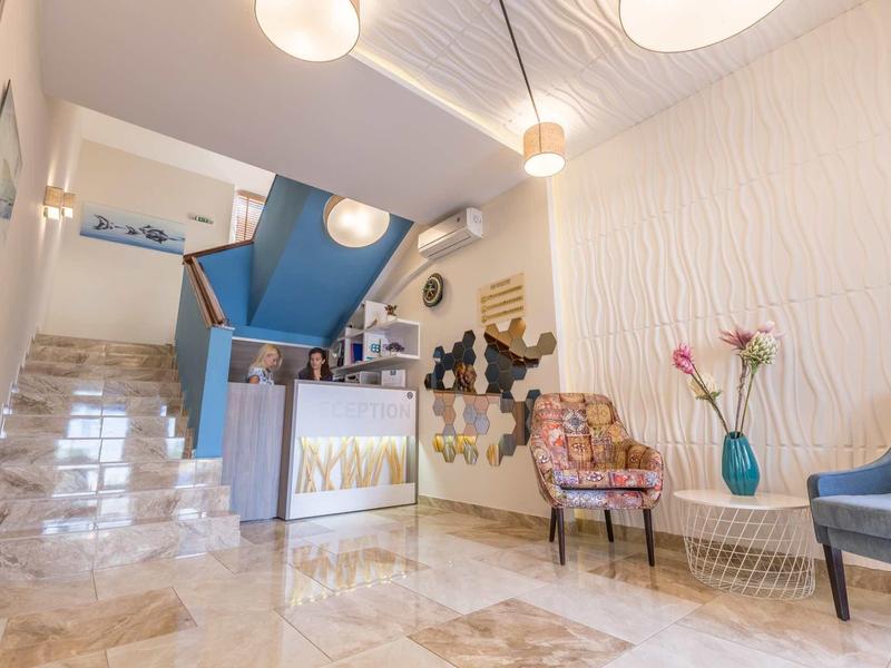 Lichte hotelgang met moderne zitplaatsen, marmeren vloer en blauwe accentmuur.