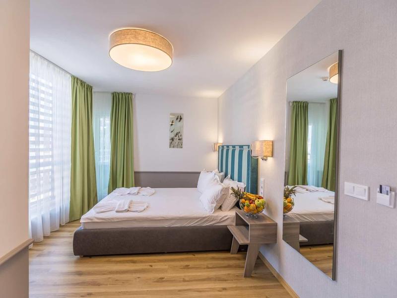 Modern hotelkamer met bed, groot raam en groene gordijnen.