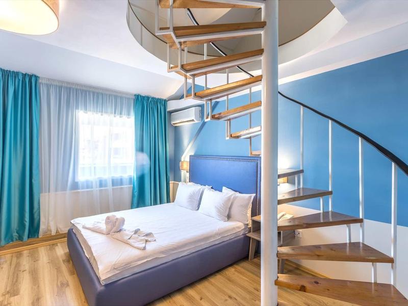Modern hotelkamer met blauw kleurenschema en wenteltrap naar een bovenverdieping.