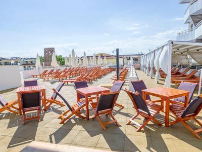 Terrace with lounge chairs and tables in a hotel pool area under a blue sky.