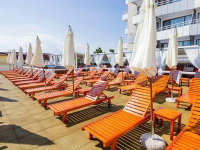 Several orange lounge chairs with white umbrellas on a terrace next to a hotel building.