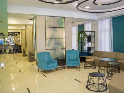 Modern hotel lounge area with blue armchairs, sofas, and an adjacent bar counter.