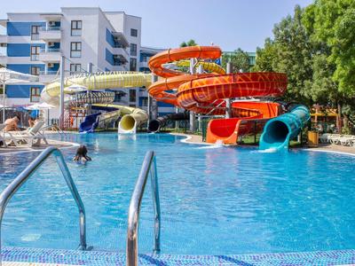 Hotel pool with colorful water slides and umbrellas next to a modern building.