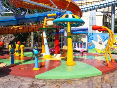 Colorful water playground with slides and sprinklers in a hotel recreational area.