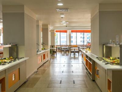 Brightly lit hotel buffet area with food on both sides and tables in the background.