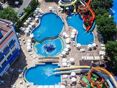 View of a hotel resort with multiple pools and colorful water slides, surrounded by lounge chairs.