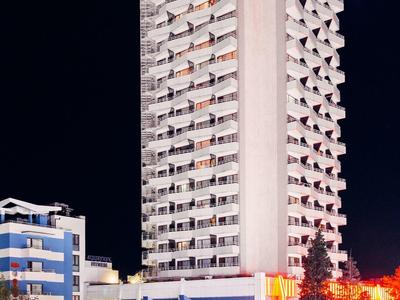 High-rise hotel building illuminated at night, surrounded by cars and nearby structures.