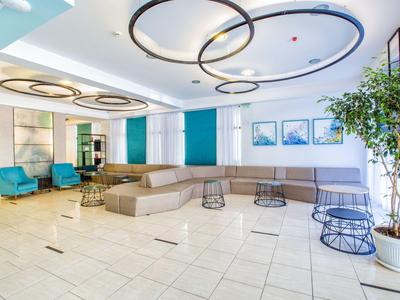 Bright lounge with modern seating, circular ceiling lights, and large windows.