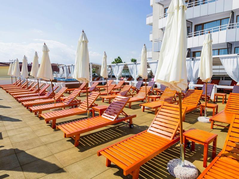Sun terrace with orange lounge chairs and white umbrellas in front of a hotel building.