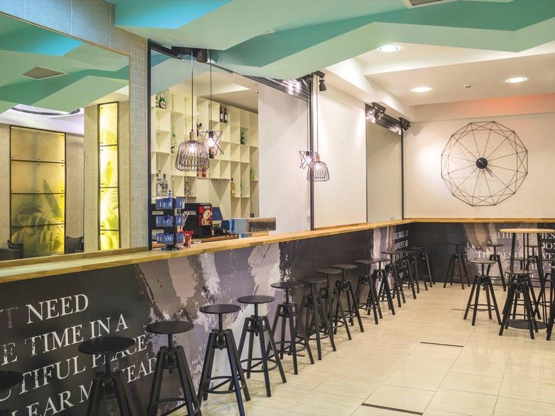 Modern hotel bar area with black counter and bar stools under geometric ceiling.