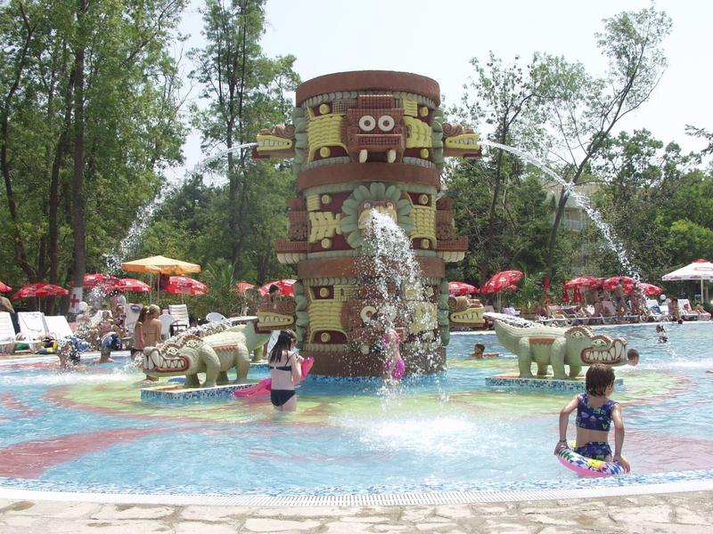 Children playing in a colorful water park with water jets and decorative elephant statues.
