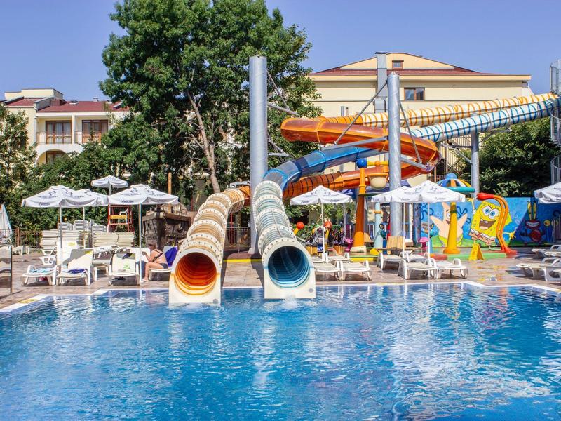Outdoor pool with water slides, sun loungers, and umbrellas in a hotel garden on a clear day.