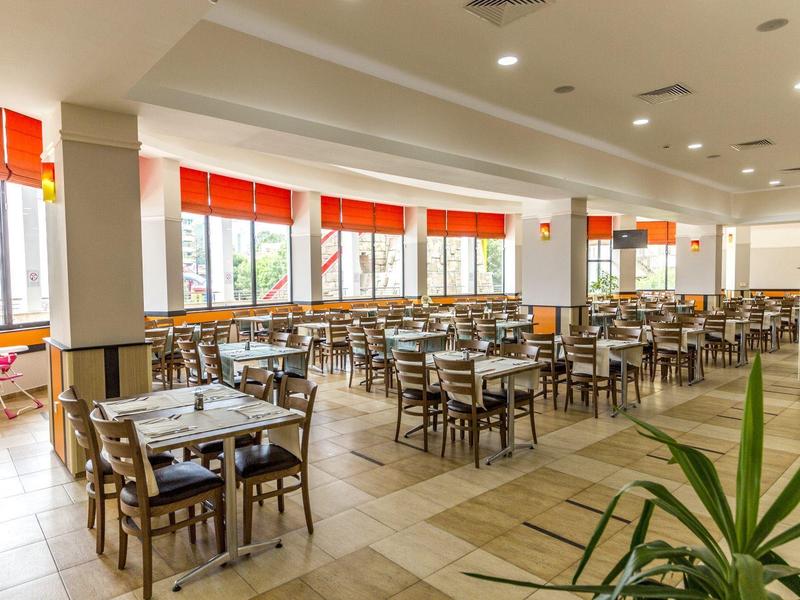 Spacious modern dining area with many tables and chairs, large windows with red curtains.