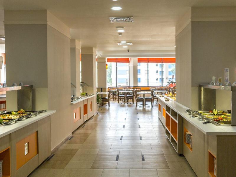 Brightly lit hotel buffet area with food on both sides and tables in the background.