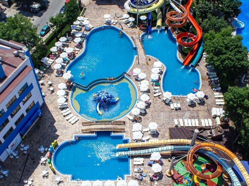 View of a hotel resort with multiple pools and colorful water slides, surrounded by lounge chairs.