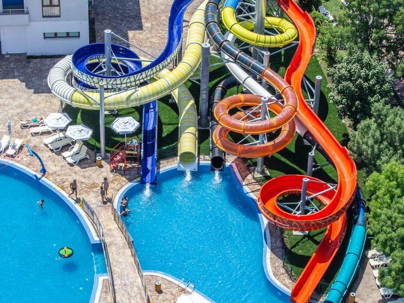 Colorful water slides over a pool in a hotel complex area.