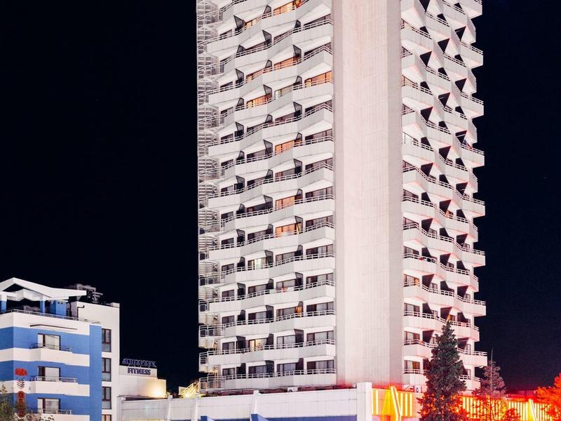 High-rise hotel building illuminated at night, surrounded by cars and nearby structures.