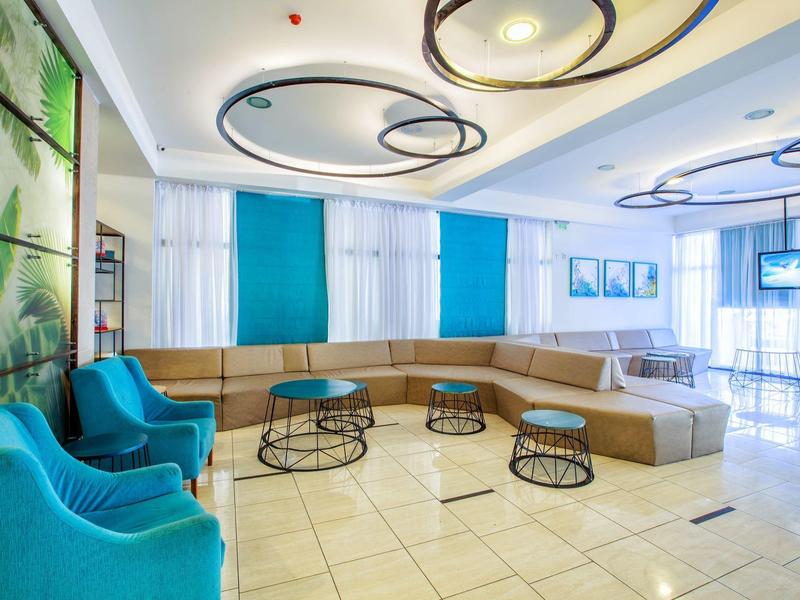 Modern hotel lobby with blue armchairs, brown sofa, and decorative ceiling lighting.