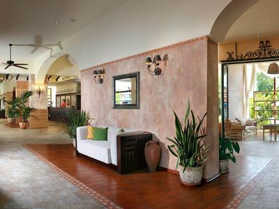 Ruime hotel lobby met zitgedeeltes, planten en toegang tot een lichte buitenruimte.