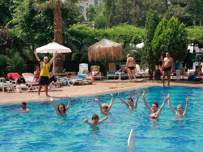 Lidé si užívají bazén v slunečný den s posezením v pozadí.