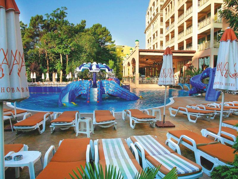 Hotelzwembad met parasols, ligstoelen en glijbanen naast een meerlaagse gebouw.