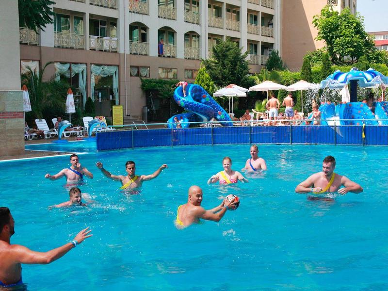 Mensen genieten van een zwembad met glijbaan voor een hotelgebouw op een zonnige dag.