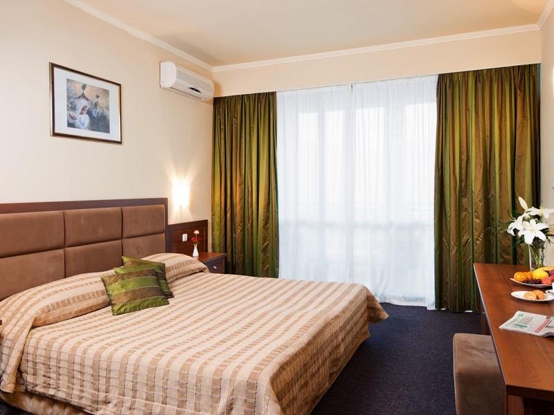 Gezellige hotelkamer met groot bed, bureau en raam met groene gordijnen.