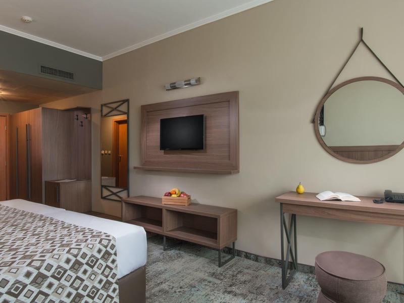 Modern hotelkamer met bed, tv, spiegel en bureau.