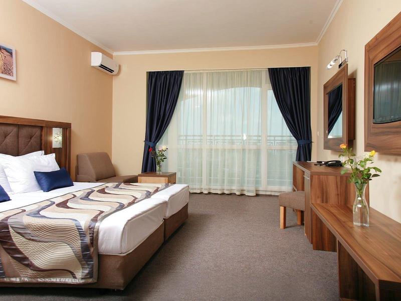 Moderne hotelkamer met twee bedden, bureau, tv en grote ramen met gordijnen.