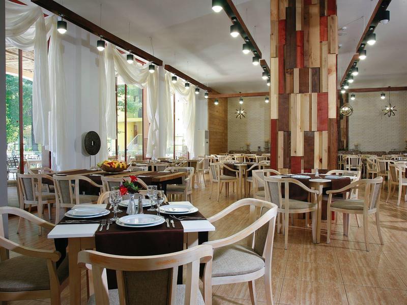 Licht restaurant met houten stoelen, ronde tafels en een lamellende zuil in het midden.