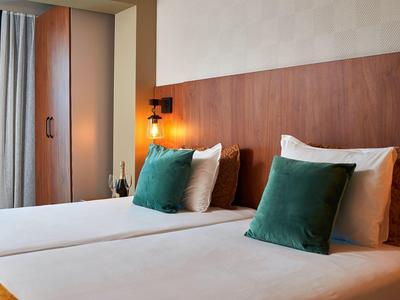 Moderne hotelkamer met twee eenpersoonsbedden, groene kussens en warme houten panelen achter het bed.