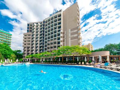 Un hotel moderno con una gran piscina al aire libre y sombrillas bajo un cielo azul.