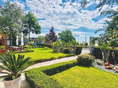 Vista de un jardín bien cuidado con césped, árboles, senderos y vista a un lago.
