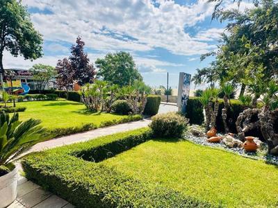 Tuin met verzorgd gazon, planten en uitzicht op zee onder een blauwe lucht met wolken.