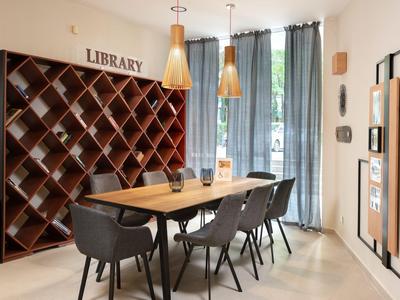Sala de lectura moderna con mesa de madera, sillas negras y estanterías de cajas de vino en la pared.