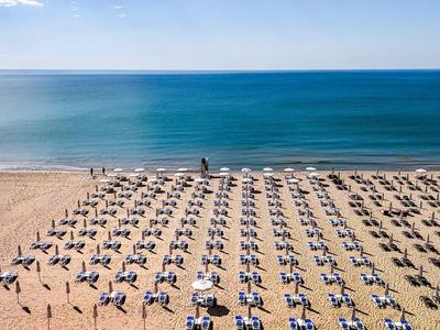 Strand mit Reihen von Liegestühlen und Sonnenschirmen am blauen Meer