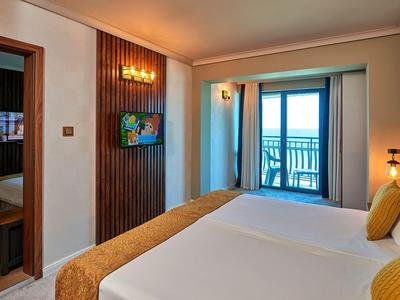 Hotelkamer met tweepersoonsbed, aan de muur gemonteerde tv en balkon met zeezicht.