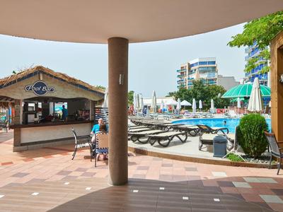Uitzicht op een hotelzwembad met ligstoelen en een bar onder een overdekt gedeelte.