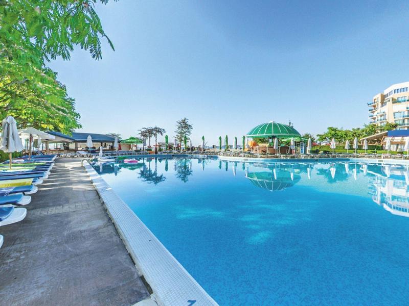 Groot buitenzwembad met ligstoelen en hotelgebouwen onder een heldere blauwe lucht