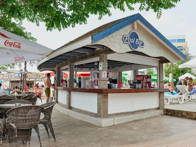 Buitenbar met zitplaatsen onder bomen en parasols in een bruisend vakantieoord.