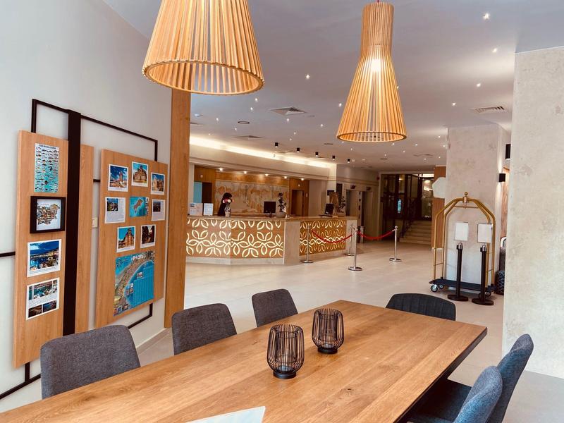 Moderne hotel lobby met receptie, houten tafel en stoelen, warme hanglampen en informatiewand.