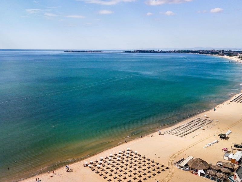 Lang zandstrand met helderblauw water en meerdere ligbedden en parasols