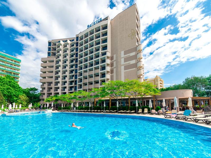 Groot hotel met buitenzwembad en ligstoelen onder een blauwe lucht.