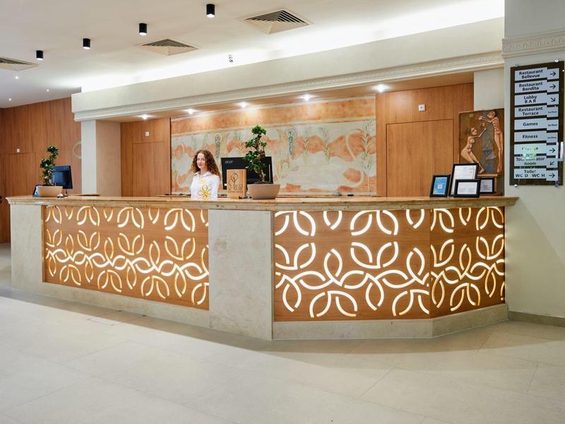 Moderne hotel receptie met verlicht houten balie en twee medewerkers.