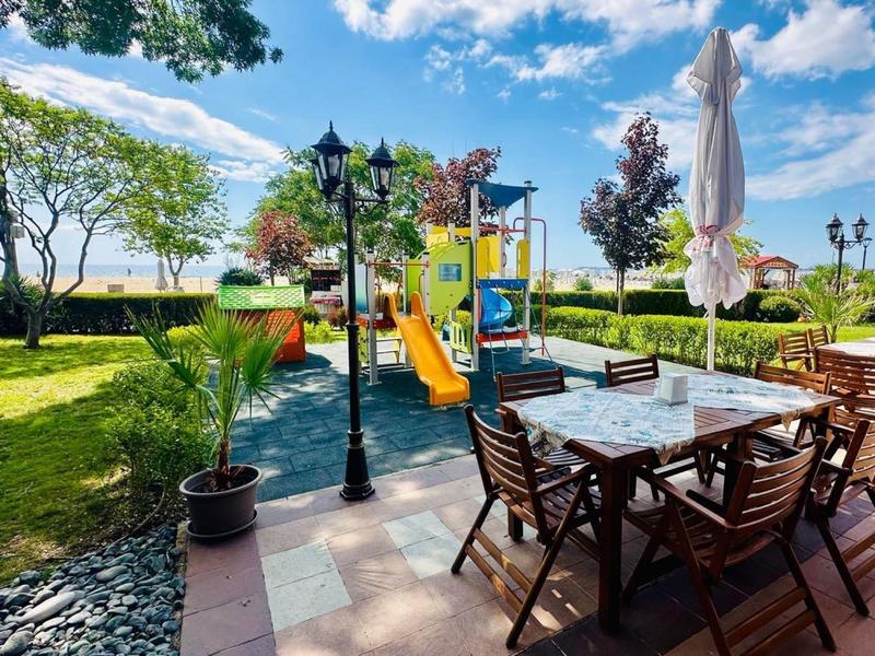 Tuin met zitplaatsen en kleurrijke speeltuin bij zonnig weer.