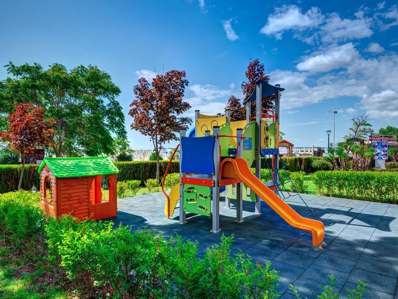 Kleurrijke speeltuin met glijbaan en klein huisje in zonnig park met blauwe lucht.