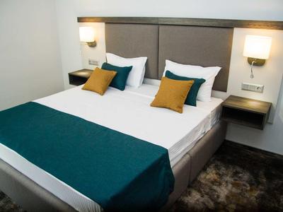 Gezellig tweepersoonsbed met grijs-blauwe loper en gele kussens in moderne hotelkamer.