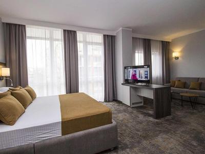 Modern hotelkamer met tweepersoonsbed, bank en groot raam met gordijnen.