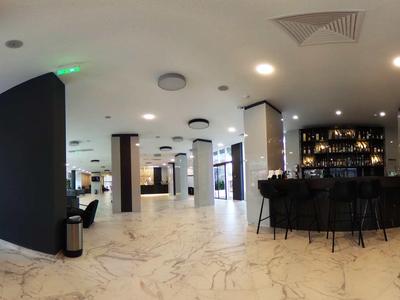 Moderna recepción de hotel con suelos de mármol blanco y barra negra en un espacio amplio y luminoso.