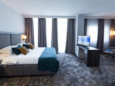 Moderne hotelkamer met groot bed, tv en zithoek in neutrale kleuren.
